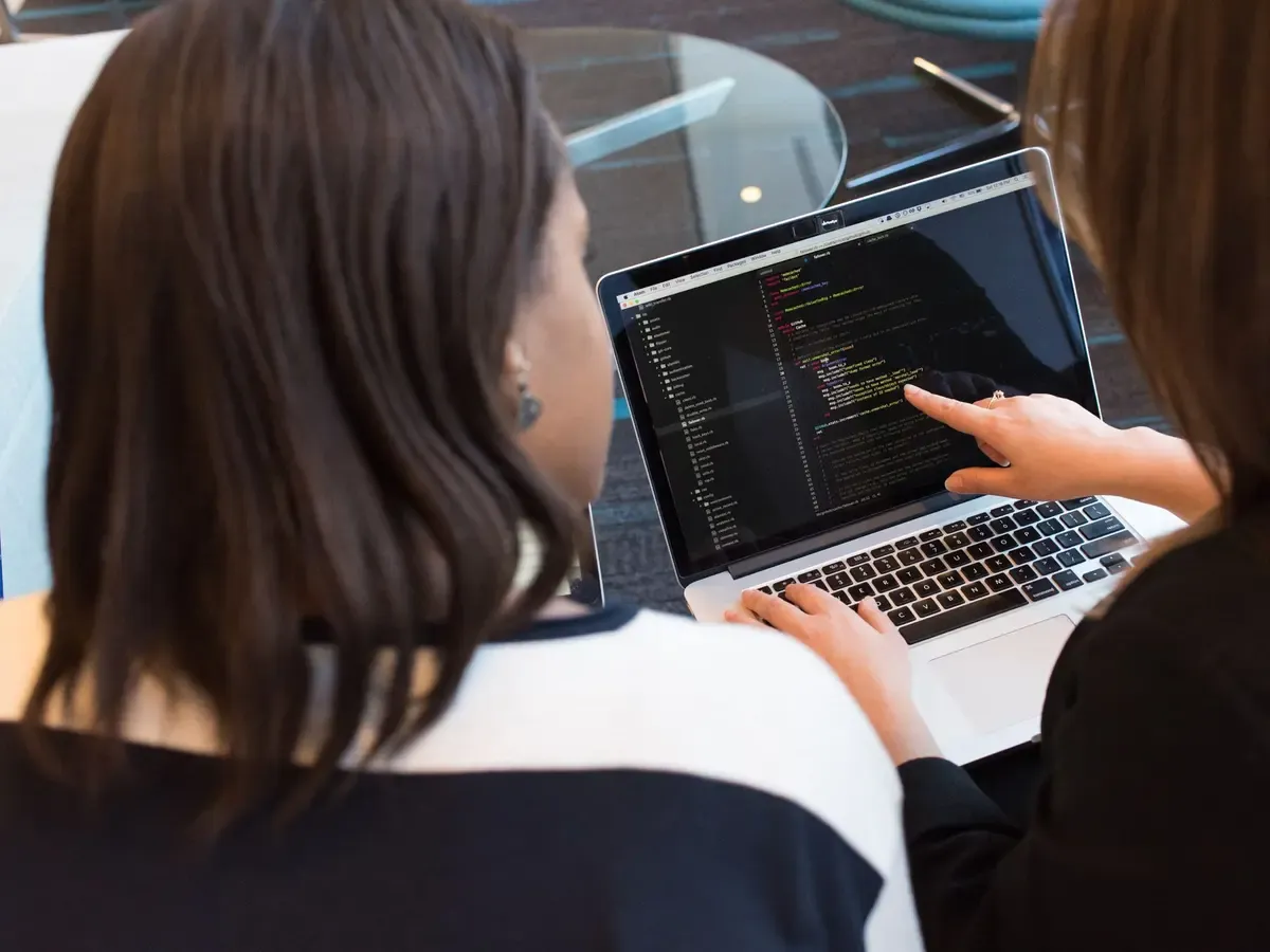 Két ember egy laptop előtt közösen átnézi a képernyőn futó kódot